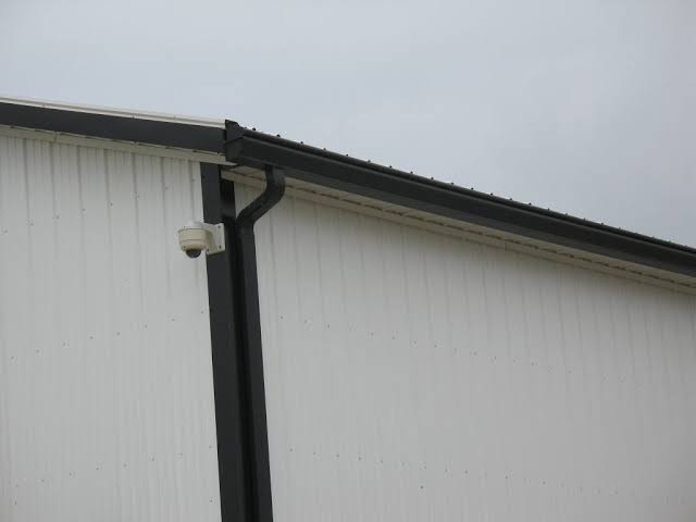 Black gutter and downspout installation on a white industrial metal building